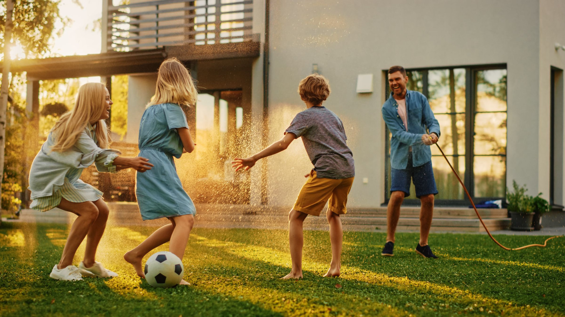 Kinder spielen mit dem Gartenschlauch vor einem modernen Haus